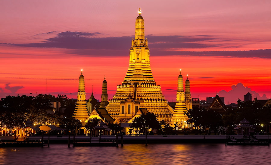Il maestoso tempio Wat Arun illuminato al tramonto lungo il fiume Chao Phraya a Bangkok